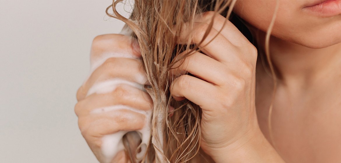 Frau shampooniert und pflegt ihre nassen blonden Haare.“
